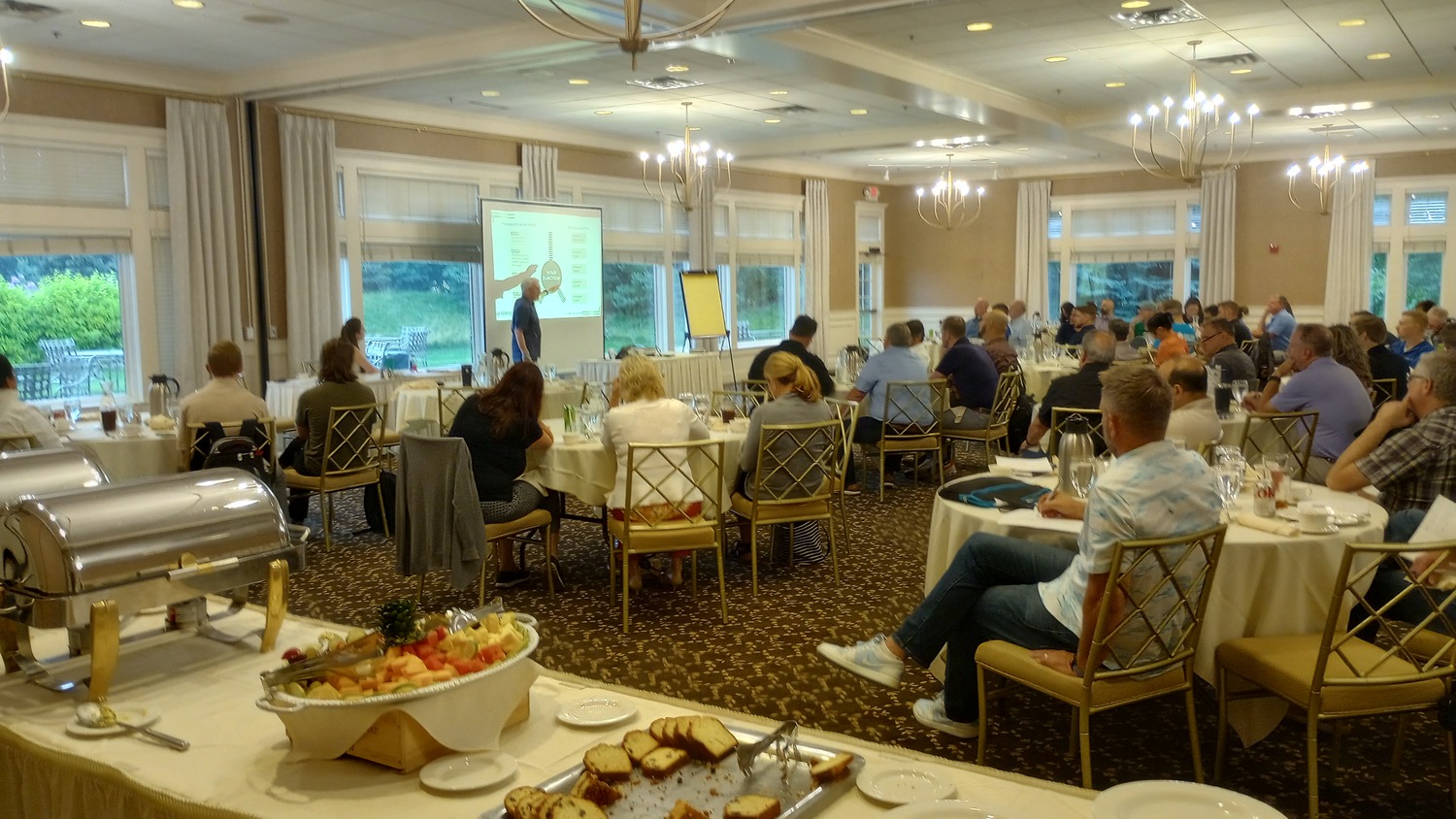 large group of people sitting around tables attending a speaking event